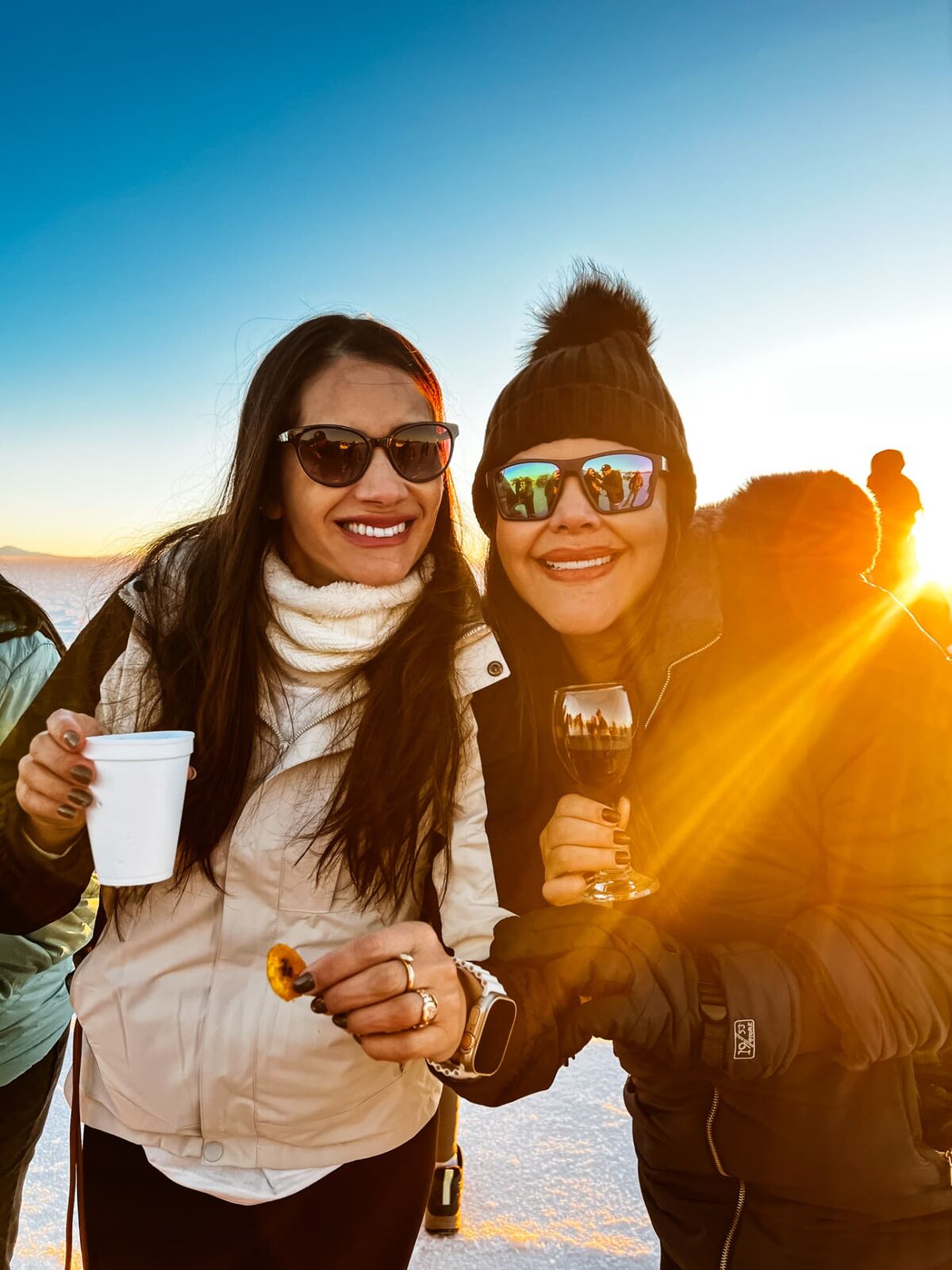Duas viajantes brindando ao pôr do sol no Salar de Uyuni